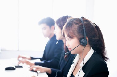 Genç melez çağrı merkezi operatörleri çalışma masasında elektronik cihazlar ve ofis malzemeleriyle modern ve rahat ofis malzemelerinin üstünde oturuyorlar.