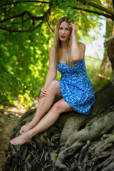 穿着蓝色衣服坐在树根上的女人 — 图库照片