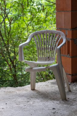 Bitmemiş bir evde arka planda ağaçlar olan kırık bir bahçe sandalyesi.