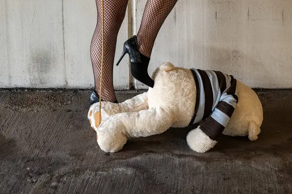 a dominatrix in black high heels gives a teddy bear a kick in the butt