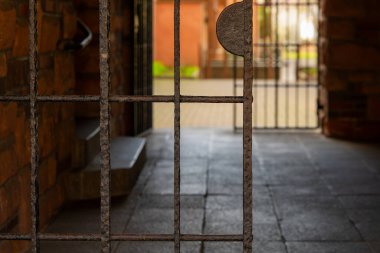 Üstünde metal bir çubuk olan paslı bir kapı. Kapı açık ve parmaklıklar görünür.