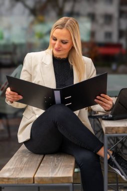 Bir iş kadını bir kafenin önünde oturur ve şehirdeki bir dosya klasörünü okur.