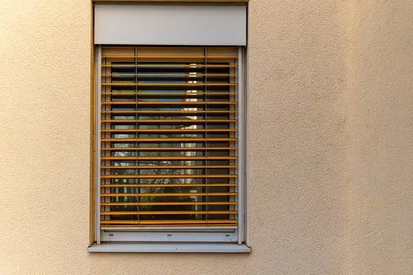 a window with wooden blinds is shown against a brown wall