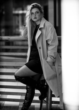 Çekici bir kadın şehirde siyah beyaz bir taburede oturuyor.