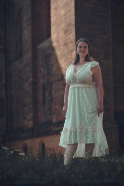 Beyaz elbiseli bir kadın binanın önünde duruyor.