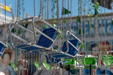 Bir sıra salıncak, yeşil ve mavi koltuklar zincirden sarkıyor.