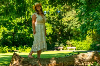 Beyaz elbiseli bir kadın parkta bir kütüğün üzerinde duruyor.