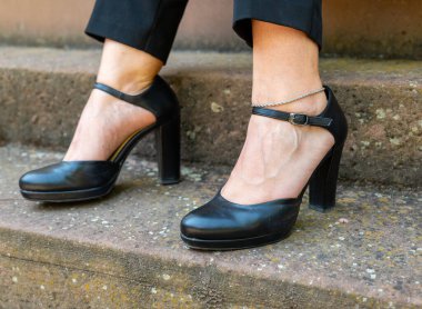 Siyah topuklu ayakkabı ve gümüş bilezik takan bir kadın. Ayakkabılar siyah ve kadın taş bir merdivende duruyor.