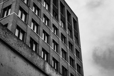 Birçok penceresi ve arka planda bulutlu bir gökyüzü olan tuğla bir bina.