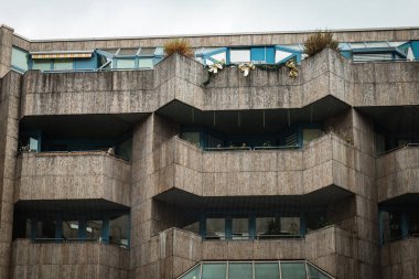 Görüntü beton bir apartmanın bir bölümünü gösteriyor. Binanın balkonları ve pencereleri olan birkaç katı var. Balkonlar betondan yapılmış ve parmaklıkları var..