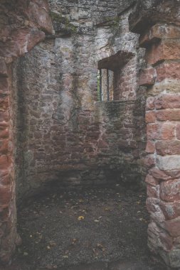 Taştan bir harabenin içinde küçük bir oda. Oda penceresiz ve kirli zemini var. Duvarda parmaklıklı bir pencere var, avluya bakıyor..