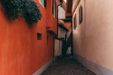 Görüntü iki yüksek bina arasında dar bir ara sokak gösteriyor, solunda kırmızı tuğla bir duvar ve sağında beyaz alçılı bir duvar var..