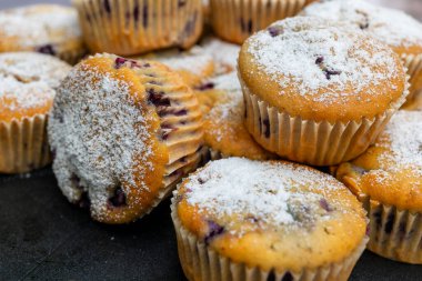 Böğürtlenli keklerin yakın plan görüntüsü, pudra şekeriyle tozlanmış. Keklerin bir kısmı diğerleri tarafından kısmen gizleniyor ve bu görüntü muffinlerin çeşitli açılarını gösteriyor..