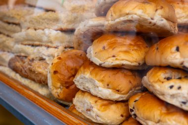 Fırının vitrininde yeni pişmiş çörekler sergileniyor. Çörekler bir yığın halinde dizilir ve altın rengi kahverengidir. Bazı çöreklerde görünür çikolata parçaları var..