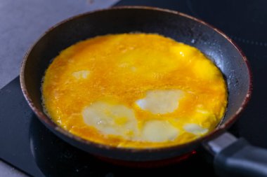 Yumurtalar siyah bir sobanın üstünde siyah bir tavada pişiyor. Yumurtalar çırpılmış ve pişmiş gibi görünüyor..