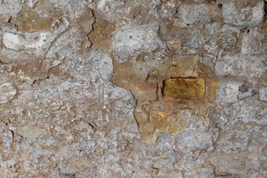 Yakından bakıldığında çatlakların oluştuğu, sert tuğlaların parçalarını ve eski malzemelerin katmanlı dokusunu ortaya çıkaran yıpranmış taş bir duvar görülüyor..