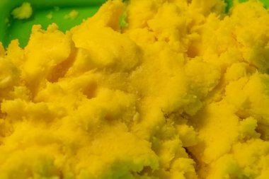 Parlak sarı tatlının canlı bir karışımı yeşil bir kabın içinde tezgahın üzerinde duruyor. Yumuşak, kabarık dokusu yakın pencerelerden gelen güneş ışığını yansıtan yeni yapıldığını gösteriyor..