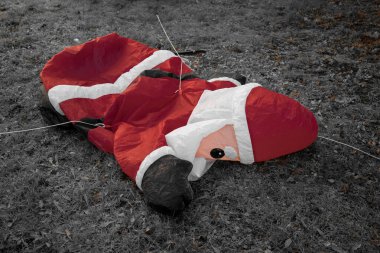 Söndürülebilir bir Noel Baba figürü yerde yatıyor. Parlak kırmızı elbisesi çimenlerin soluk renkleriyle çelişiyor. Terk edilmiş görünüyor, neşeli bir neşesi yok..