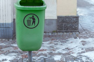 Çöp öğütme için tasarlanmış yeşil bir çöp kutusu karlı bir kaldırım taşı caddesine yerleştirildi. Çöp kutusunda uygun atık yönetimi ve geri dönüşümü teşvik eden bir sembol yer alıyor