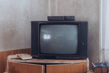 Eski bir televizyon, duvarları ve dağınık eşyaları soyarak karakterize edilen bir odadaki ahşap bir dolabın üzerine yerleştirilir. Bu iç mekan ortamında yıllar süren terk edilmişlik ve ihmalkârlık.