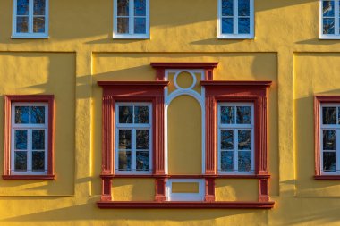 Çarpıcı sarı bir bina, yaratıcı bir mimari stili vurgulayan kırmızı pencere çerçevelerine sahiptir. Güneş ışığı ön cephede güzel gölgeler bırakıyor..