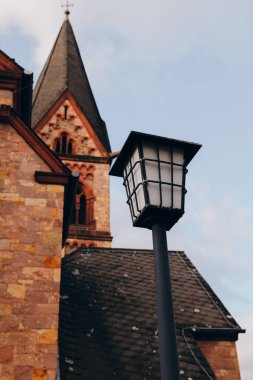 Tarihi bir kilisenin önünde duran klasik bir sokak lambası karmaşık taş işçiliği ve uzun bir kule ile öğleden sonra güneşinin altında güzel bir manzara yaratıyor..