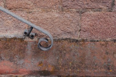 Yakından bakıldığında, yıpranmış taş bir duvara tutturulmuş şekillendirilmiş demir parmaklıklar görülüyor. Dokuların birleşimi, yapının işçiliğini ve yaşını vurgular..