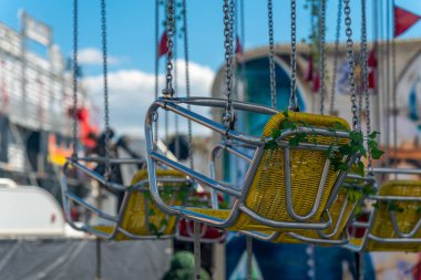 Güneş ışığıyla aydınlatılan bir lunaparkta renkli koltuklar askıya alınır. Park etkinliklerle dolu. Neşeli ziyaretçilerin kahkahaları yazın tadını çıkarıyor..