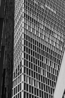 Yapı, modern tasarım ilkelerini yansıtan karmaşık bir pencere ve metal şebeke deseni sergiliyor. Açık gökyüzünün altında hareketli bir şehir siluetinde yer almaktadır..