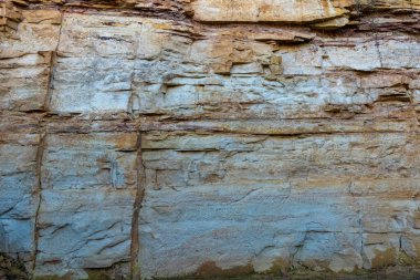 Sabahın erken saatlerinde güneybatıdaki bir kaya yüzeyinde çarpıcı renkli kil katmanları ortaya çıkar. Doku ve renkler jeolojik özellikleri ve desenleri vurgular.