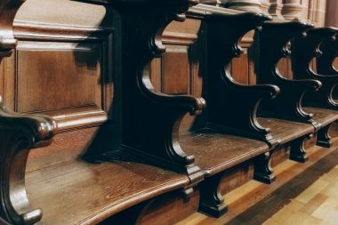 Parlak ahşap kilise sıralarının detaylı görüntüsü tarihi bir tapınakta dizilmiş, süslü oymaların işçiliğini gözler önüne seriyor. Sıcak tonlar dingin bir atmosfer ekler..