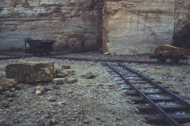 An abandoned quarry reveals rusted cart tracks and mining equipment against rugged stone walls. The atmosphere reflects a historical mining site frozen in time. clipart