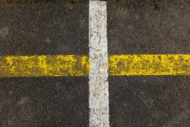 Yüzey, yayalar için yaya geçidi oluşturan soluk sarı ve beyaz çizgilere sahiptir. Asfaltın dokusunu yakalar, aşınma ve kullanım izleri gösterir..