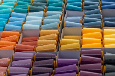 Parlak renkli ipliklerin çeşitli makaraları bir el sanatları mağazasında kutularda düzenli olarak düzenlenir. Canlı renkler, dikiş meraklıları için görsel olarak çekici bir görüntü oluşturuyor..