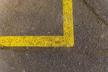 Parlak sarı bir çizgi yıpranmış beton bir yüzey üzerinde açık bir köşe işareti yaratır. Bu çizgi, gündüz saatlerinde kalabalık bir şehir ortamında belirlenmiş park yerlerini gösteriyor..