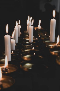 Soft, flickering candlelight illuminates a tranquil space filled with various candles, creating a peaceful ambiance during a communal evening prayer gathering.