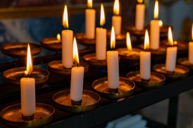 Flickering flames of white candles cast a warm glow in a peaceful religious space. The arrangement creates a tranquil atmosphere, inviting moments of reflection and prayer.