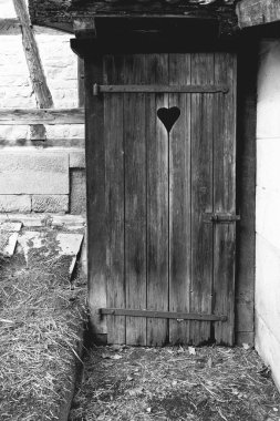 Yıpranmış ahşap bir kapı, eski bir ahırda duruyor. Kapı kırsal çevre tarafından tamamlanmış, nostalji hissi uyandırıyor..