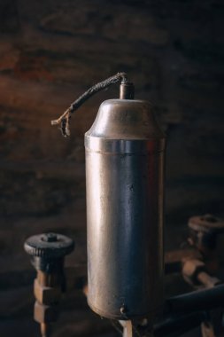 Yıpranmış bir metal sprey teneke kutu kırsal bir tezgahın üzerinde duruyor, desenli bir duvara gölge düşürüyor. Yakınlarda, çeşitli araçlar geçmiş projeler ve zanaatkarlık hakkında ipuçları veriyor.