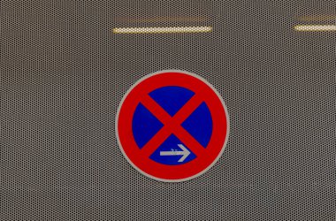 Dairesel park levhası yok. Kırmızı kenarlı ve mavi ortasında büyük bir X var. Bir ok araçların sağa dönmesi gerektiğini gösterir. İşaret delinmiş metalin üzerine asılmış..