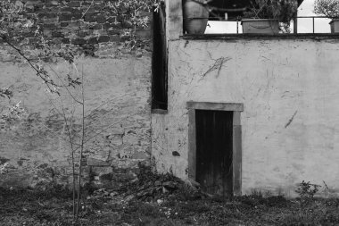 Sessiz, terk edilmiş bir alanda eskimiş taştan bir duvar ve karanlık bir kapı var. Bereketli yeşillik yakınlarda yetişiyor, bu da doğanın mekanı geri aldığını gösteriyor. Güneş ışığı dokuları vurgular.