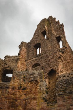 Bu çarpıcı yapı, yıkılan taş duvarları ve kemerli pencereleri olan bir ortaçağ kalesinin kalıntılarını sergiliyor. Bulutlu gökyüzü tarihi mekan için dramatik bir zemin sağlıyor.