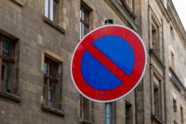 Canlı, mavi daireli ve kırmızı kenarlı park yasağı işareti klasik bir binanın hemen yanında yer alıyor. Şehir yaşamını, mimari ve yönetmelikleri yansıtıyor..
