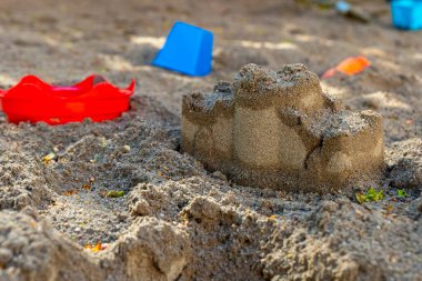 Çocuklar güneşli bir günün tadını çıkarıyorlar. Havada kahkahalar yankılanırken yumuşak kuma saçılmış renkli oyuncaklarla dolu bir oyun alanında detaylı bir kumdan kale yapıyorlar..