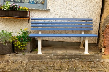 Huzurlu bir ara sokakta canlı çiçeklerle çevrili dokulu bir duvarın yanında mavi ahşap bir bank bulunur. Bu davet noktası güneşli bir günde derin düşüncelere ve rahatlamaya davetiye çıkarır..