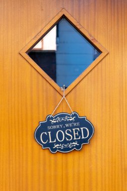 Büyüleyici ahşap bir kapı, gece ışığıyla hafifçe aydınlatılan ve kapalı okunan karanlık bir işaret içerir. Elmas şekilli pencere boş bir iç mekan ortaya çıkarıyor, sakin atmosferi güçlendiriyor..