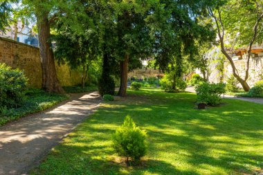 Güneş ışığı yükselen ağaçların arasından süzülür, yemyeşil çimlerin üzerine neşeli gölgeler bırakır. Bu huzurlu bahçe vahasında ziyaretçilere yol gösteren eğimli yollar yansıma için mükemmel anlar yaratıyor..