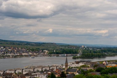Huzurlu bir manzara, nehir kenarındaki bir köyü ilginç binalar ve uzak dönme dolaplarla donatır..