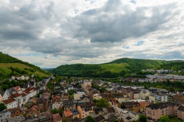 Manzaralı bir manzara, dramatik bulutlarla dolu bir gökyüzünün altında yemyeşil tepelerle çevrili pitoresk bir köy gösteriyor. Büyüleyici çatılar keşfe ve maceraya davetiye çıkarır..