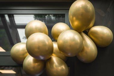 Işıldayan altın balon koleksiyonu büyük bir pencerenin yanında büyüleyici bir düzenleme oluşturur. Işık, neşeli bir toplantının atmosferini yükselterek, şenlik dekorunu aydınlatıyor..